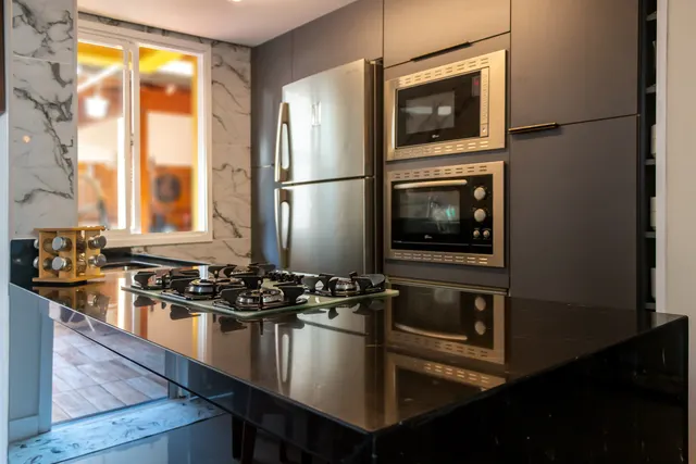 Bancada preta com cooktop em cozinha planejada grafite, com forno e micro-ondas embutidos ao lado da geladeira